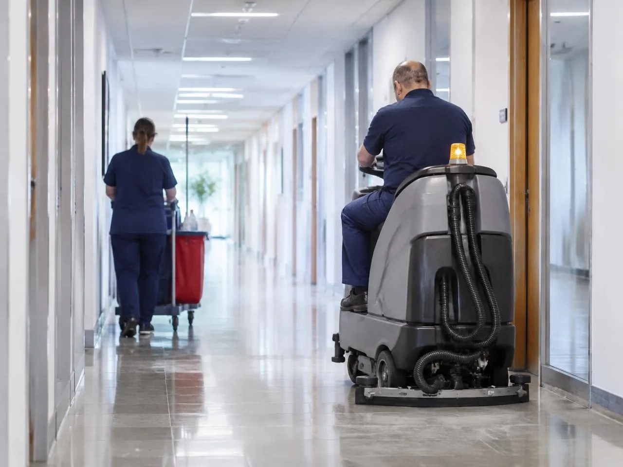Deux agents en intervention dans un couloir professionnel, autolaveuse et chariot de ménage — visuel illustratif généré